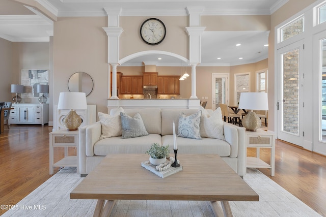 living area featuring crown molding, light wood-type flooring, and ornate columns