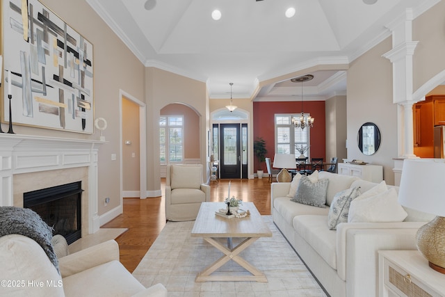 living room with light wood-type flooring, a fireplace, ornamental molding, and a raised ceiling