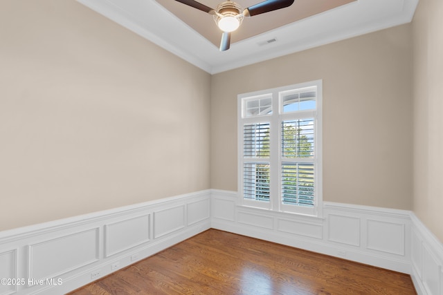 empty room featuring wainscoting, visible vents, ceiling fan, and wood finished floors