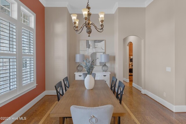 dining room with baseboards, arched walkways, light wood-style flooring, crown molding, and a notable chandelier