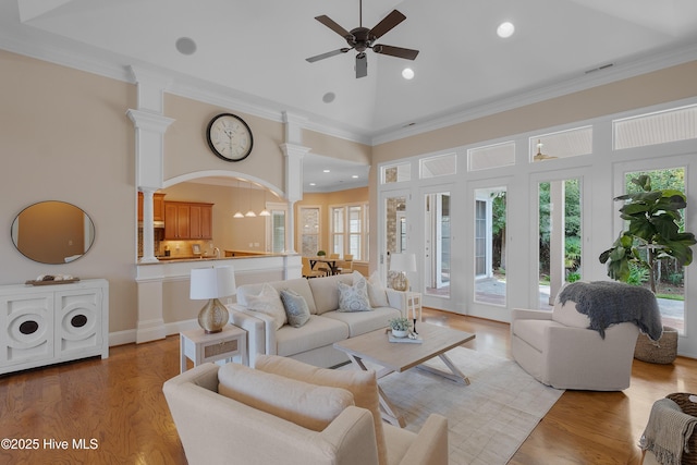 living room featuring visible vents, ornate columns, crown molding, light wood-style floors, and high vaulted ceiling