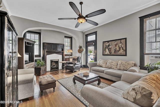 living room with ceiling fan, ornamental molding, a brick fireplace, and light hardwood / wood-style flooring