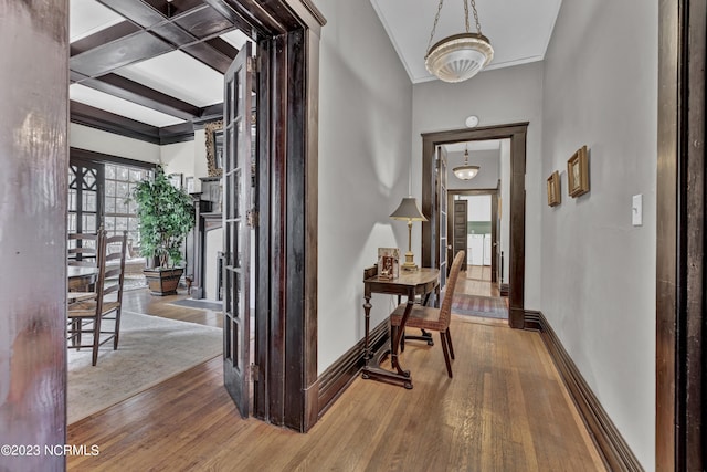 hallway with beam ceiling, crown molding, baseboards, and wood finished floors