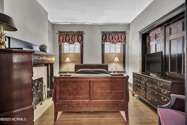 bedroom with light wood-style floors, a fireplace, and crown molding