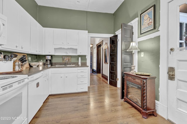 kitchen featuring white appliances, a sink, white cabinets, light wood-type flooring, and dark countertops