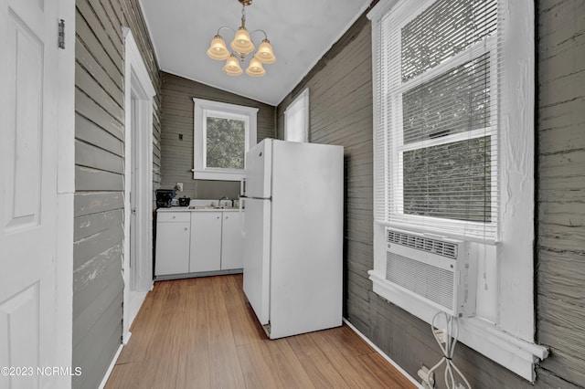 kitchen featuring wooden walls, white cabinets, decorative light fixtures, vaulted ceiling, and white fridge