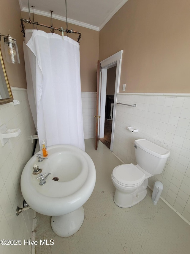 bathroom featuring toilet, ornamental molding, a wainscoted wall, and tile walls