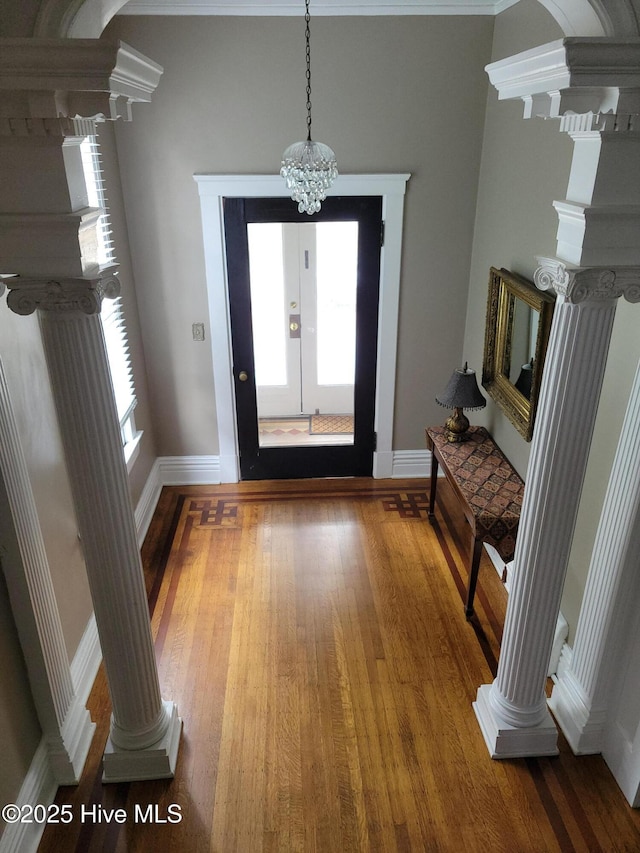 foyer with decorative columns, a notable chandelier, baseboards, and wood finished floors