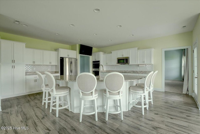 2022 Tarpon Trl, New Bern, NC 28562 - kitchen with appliances with stainless steel finishes, tasteful backsplash, a large island with sink, white cabinetry, and light wood finished floors