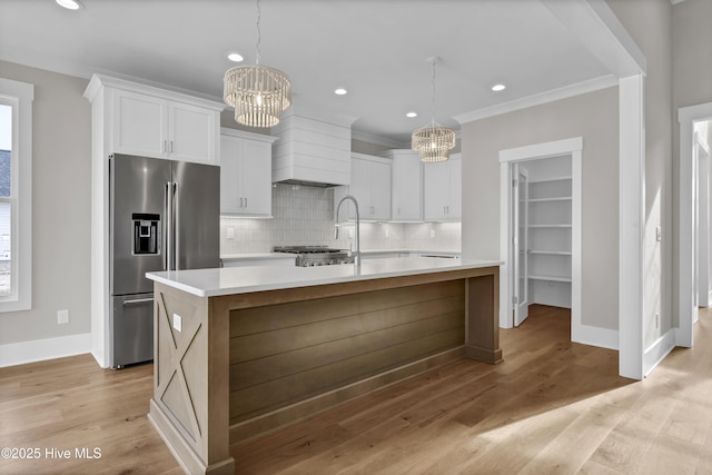 kitchen featuring hanging light fixtures, an inviting chandelier, a large island with sink, high quality fridge, and white cabinets