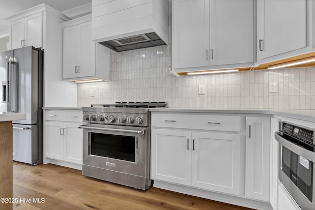 kitchen with light hardwood / wood-style flooring, premium range hood, backsplash, white cabinets, and high end appliances