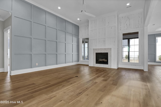 unfurnished living room featuring ceiling fan, a large fireplace, light hardwood / wood-style flooring, and ornamental molding