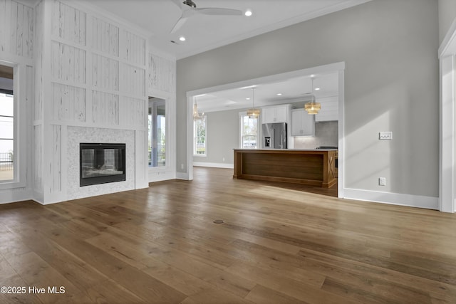 unfurnished living room featuring dark hardwood / wood-style floors, ceiling fan, crown molding, and a tiled fireplace