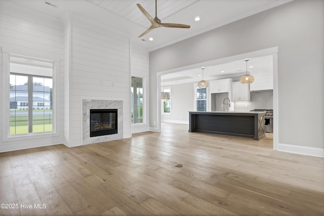 unfurnished living room with a fireplace, light hardwood / wood-style flooring, ceiling fan, and sink