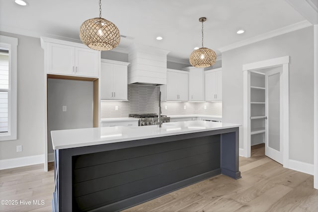 kitchen with white cabinets, custom range hood, a center island with sink, and decorative light fixtures