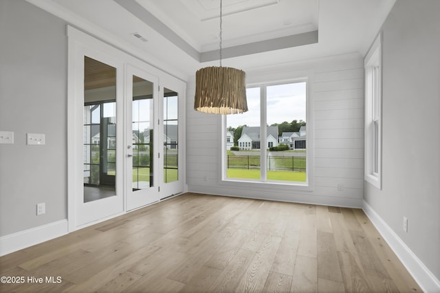 unfurnished dining area featuring a tray ceiling, light hardwood / wood-style flooring, french doors, and ornamental molding