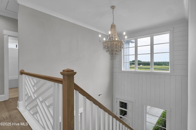 staircase with crown molding, wood-type flooring, and an inviting chandelier