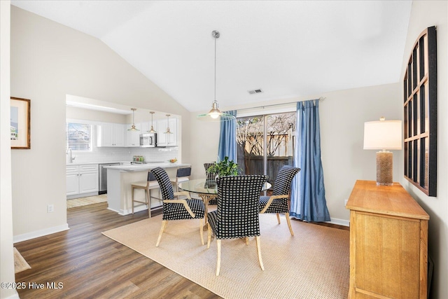 dining area featuring a healthy amount of sunlight, dark hardwood / wood-style flooring, sink, and vaulted ceiling