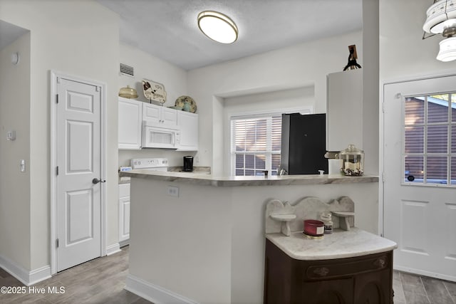 kitchen featuring kitchen peninsula, stainless steel fridge, light wood-type flooring, and white cabinetry