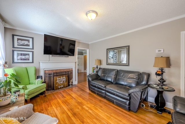 living room featuring wood-type flooring, ornamental molding, a textured ceiling, and a brick fireplace