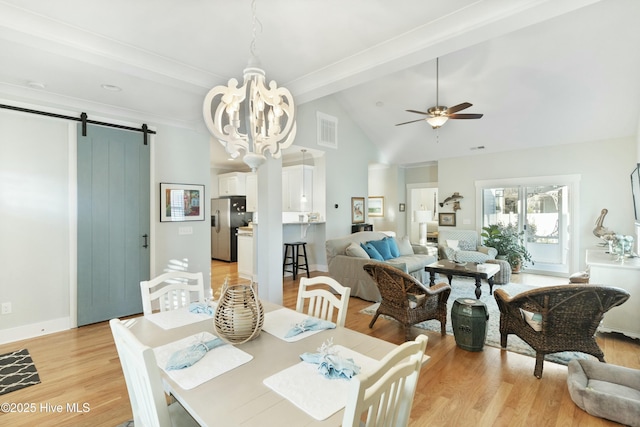 dining area featuring ceiling fan with notable chandelier, vaulted ceiling with beams, a barn door, and light hardwood / wood-style floors