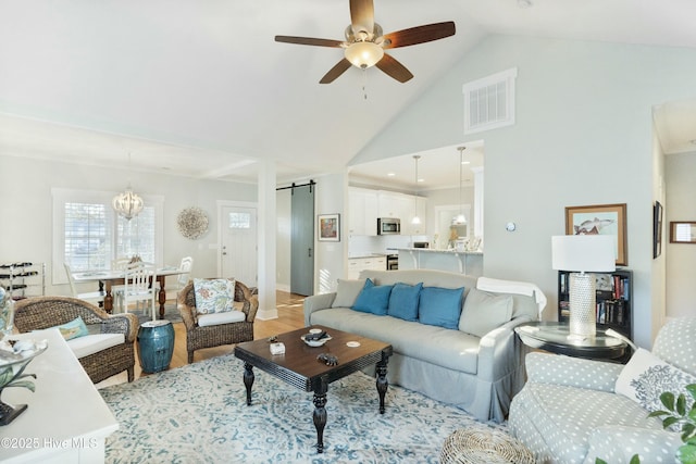 living room with a barn door, lofted ceiling, light hardwood / wood-style floors, and ceiling fan with notable chandelier