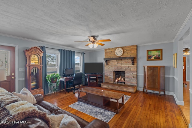 living room featuring a textured ceiling, ceiling fan, crown molding, a fireplace, and hardwood / wood-style floors