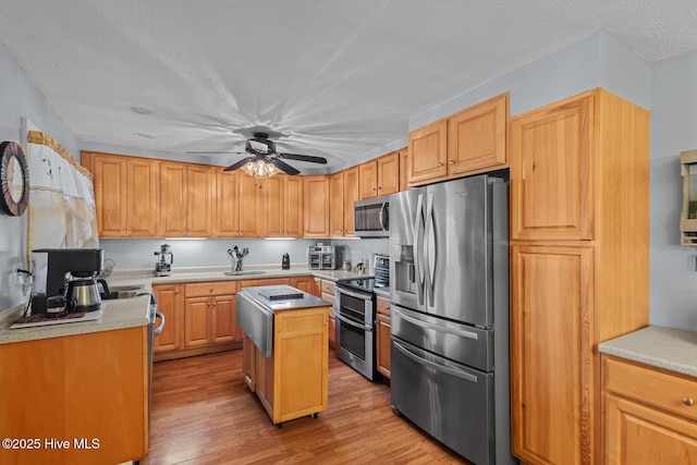 kitchen with appliances with stainless steel finishes, a textured ceiling, ceiling fan, a center island, and light hardwood / wood-style floors