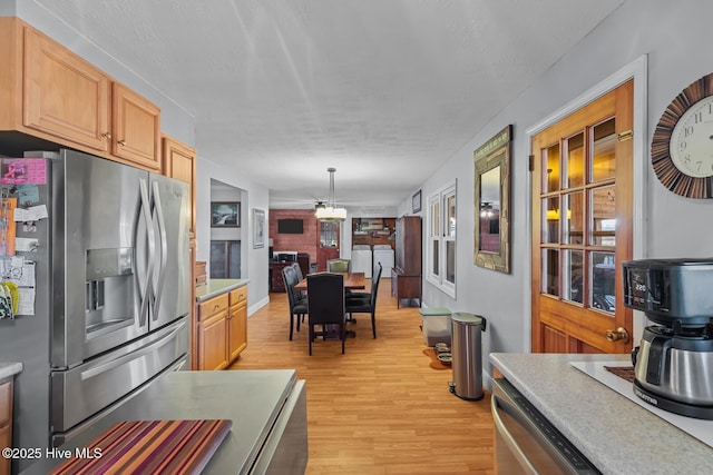 kitchen featuring light brown cabinets, stainless steel fridge, pendant lighting, stacked washer / drying machine, and light hardwood / wood-style floors