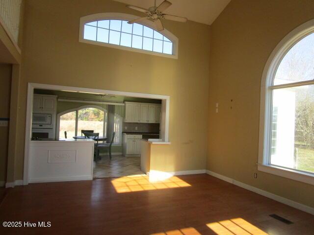 unfurnished living room featuring visible vents, a towering ceiling, light wood-style floors, ceiling fan, and baseboards