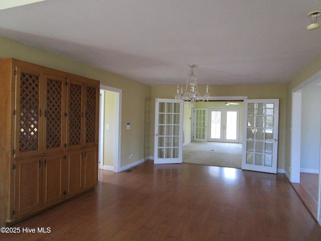 unfurnished dining area featuring french doors, a chandelier, and dark wood-type flooring