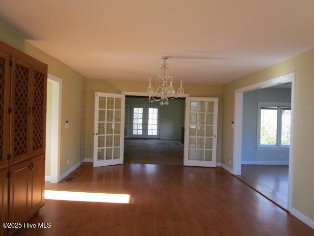 unfurnished dining area with french doors, a notable chandelier, baseboards, and wood finished floors