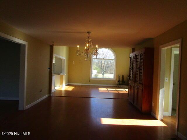 unfurnished dining area featuring wood finished floors, baseboards, and an inviting chandelier