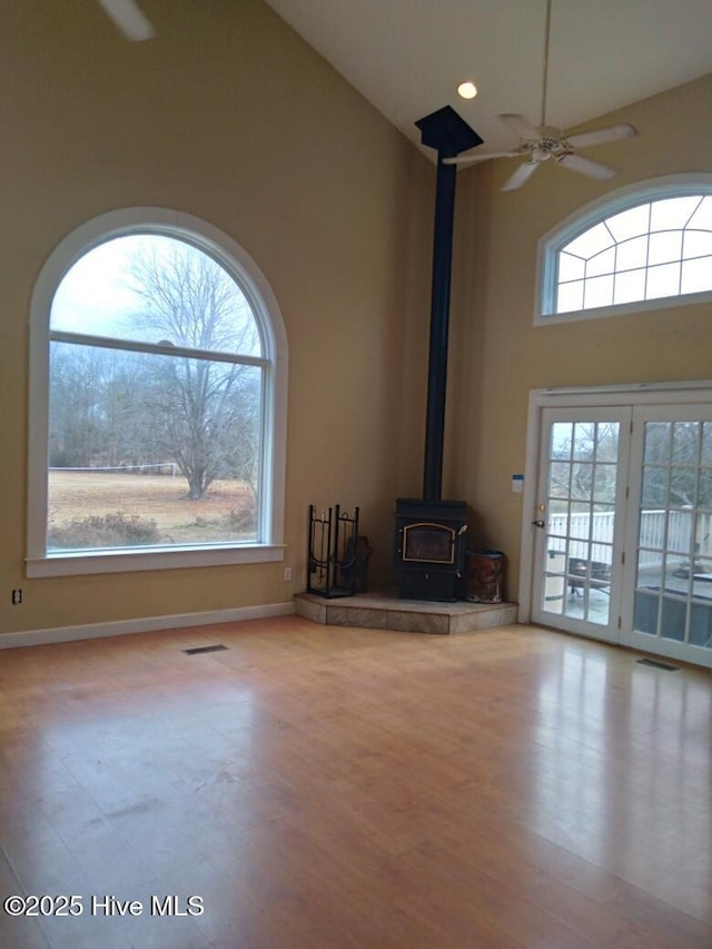 unfurnished living room with a towering ceiling, light wood-type flooring, ceiling fan, and a wood stove