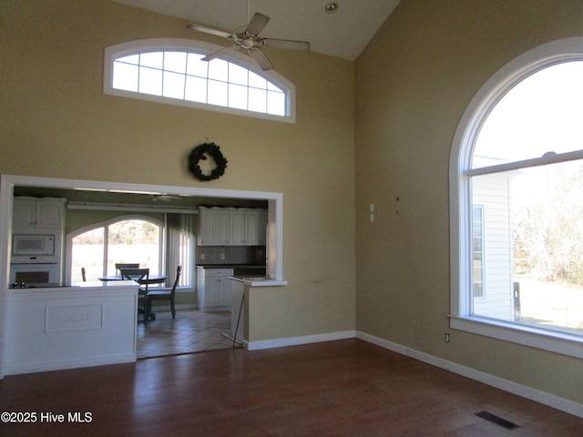 interior space with dark hardwood / wood-style flooring, a towering ceiling, and ceiling fan