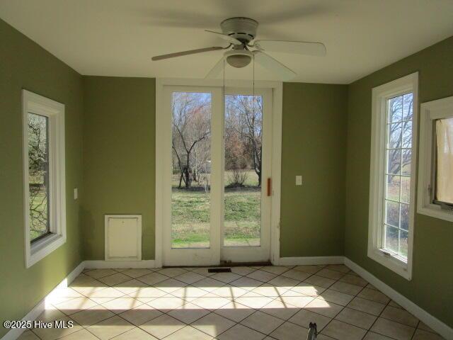 doorway featuring light tile patterned floors, ceiling fan, a wealth of natural light, and baseboards