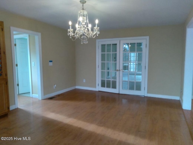 spare room featuring baseboards, a chandelier, wood finished floors, and french doors