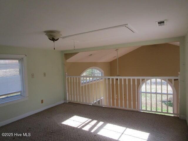 carpeted empty room featuring visible vents, vaulted ceiling, and baseboards