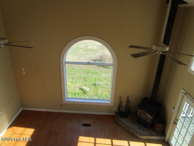 unfurnished living room with visible vents, baseboards, ceiling fan, wood finished floors, and a wood stove