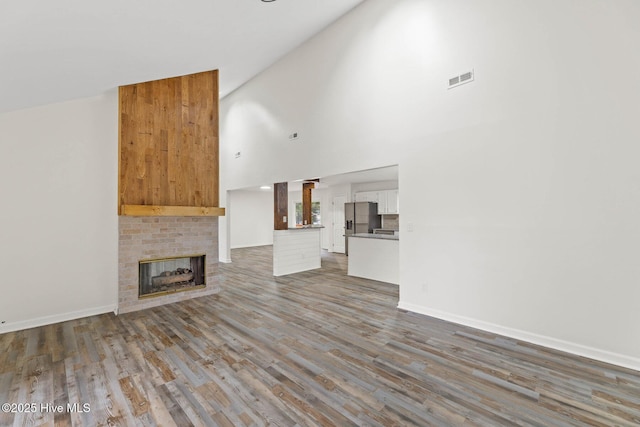 unfurnished living room featuring high vaulted ceiling, hardwood / wood-style flooring, and a brick fireplace