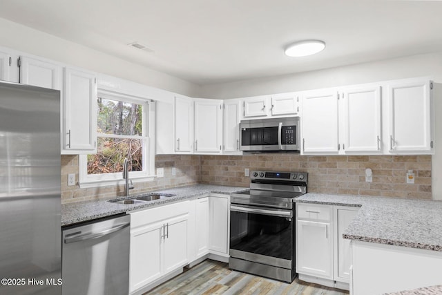 kitchen with light stone countertops, stainless steel appliances, sink, light hardwood / wood-style flooring, and white cabinets