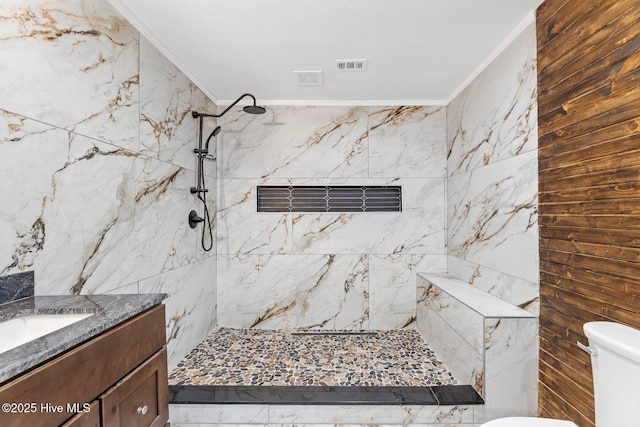 bathroom with vanity, toilet, ornamental molding, and tiled shower