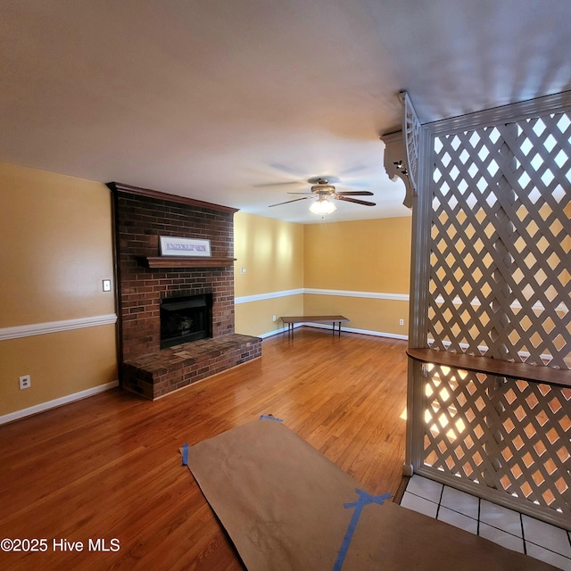 unfurnished living room with ceiling fan, wood-type flooring, and a brick fireplace