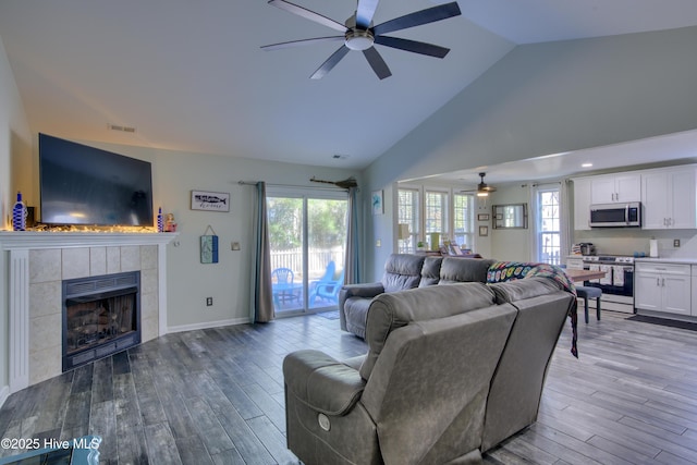 living room with ceiling fan, wood-type flooring, and a tiled fireplace