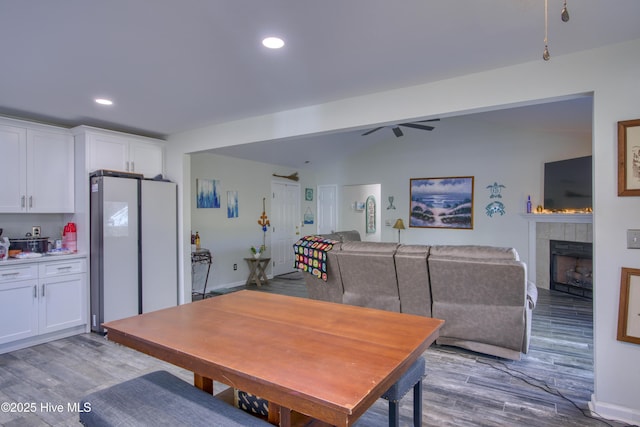 dining room featuring light wood-type flooring, ceiling fan, and a tiled fireplace