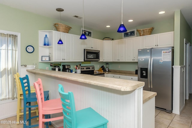 kitchen featuring a kitchen breakfast bar, kitchen peninsula, hanging light fixtures, appliances with stainless steel finishes, and white cabinetry