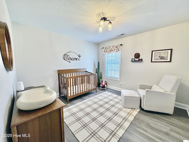 bedroom featuring wood-type flooring, a textured ceiling, and a crib