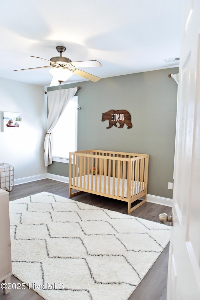 bedroom with dark hardwood / wood-style flooring, a nursery area, and ceiling fan