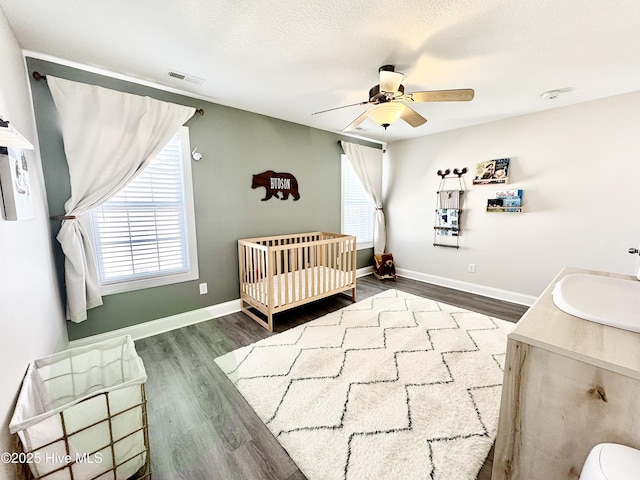 bedroom with a nursery area, hardwood / wood-style floors, sink, ceiling fan, and a textured ceiling