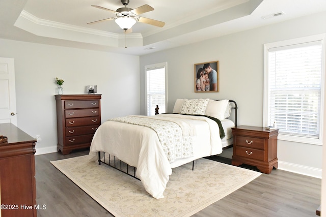 bedroom featuring hardwood / wood-style flooring, multiple windows, ceiling fan, and a tray ceiling